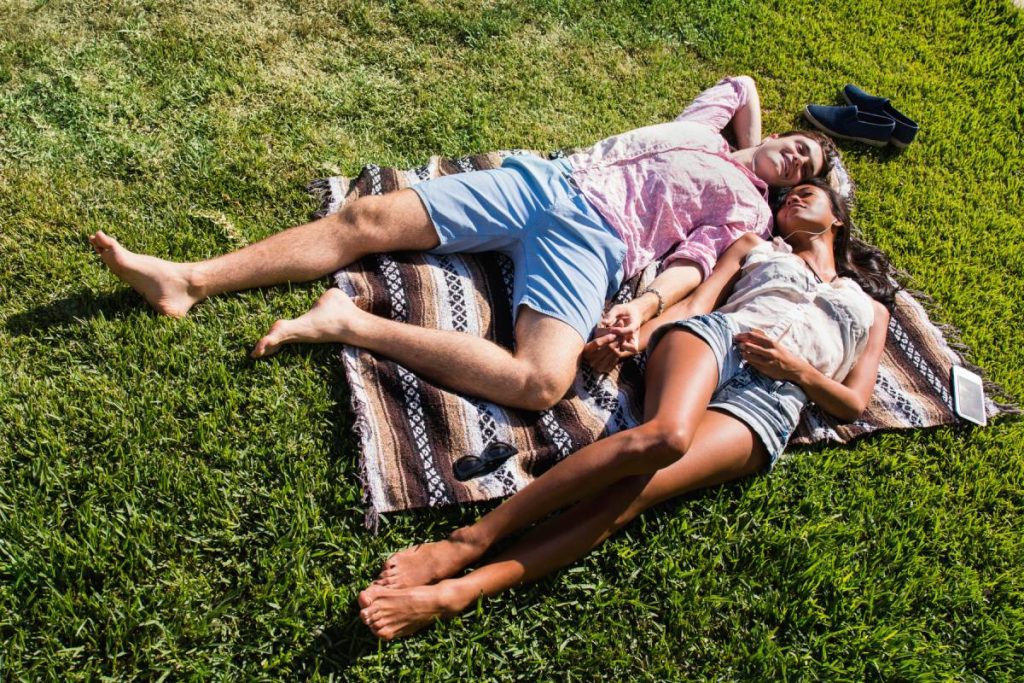 Young couple relaxing outdoors, lying on blanket on wintergreen couch, sharing earphones